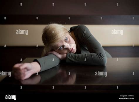 Blonde Woman Looking Sad Leaning Her Body Over A Table In A Bar Stock