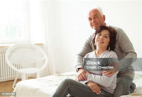 Mature 60 Year Old Couple Hugging While Sitting On The Bed In The