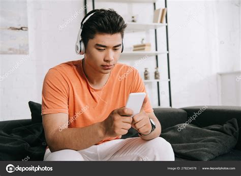 Thoughtful Asian Man Listening Music Headphones Using Smartphone While