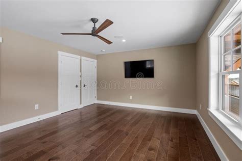 Empty Room With A Ceiling Fan Hardwood Floor And Large Windows Stock