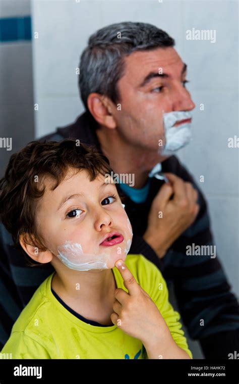 Father And Son Are Applying Shaving Foam On Their Faces In Bathroom A