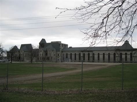 A Large Building Behind A Chain Link Fence With Trees In The Foreground