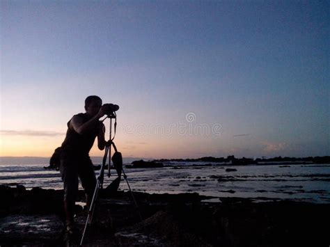 Silhouette Of A Photographer Capturing A Scenic Coastal Sunrise