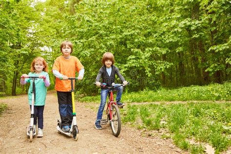 Three Kids With Scooter And Bike In The Park Stock Photo Image Of