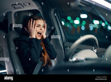 Frightened Woman Is Sitting Behind The Wheel Of A Car In A Black Shirt Wearing A Seat Belt