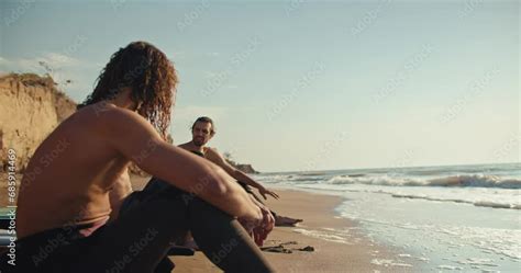 Three Surfer Guys With Naked Torsos Sit On The Seashore On Sandy Beach