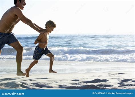 Father And Son Running Along Beach Together Wearing Swimming Costumes