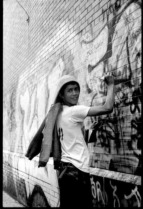 A Man Standing Next To A Brick Wall Covered In Graffitti And Writing On It