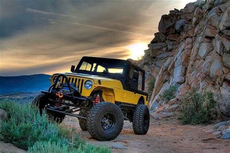 A Yellow Jeep Is Parked On The Side Of A Rocky Road Near Some Grass And Rocks