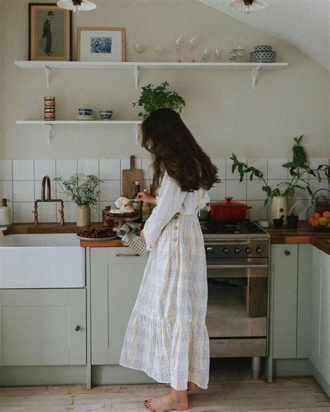 A Woman In A White Dress Is Standing At The Kitchen Counter And Looking