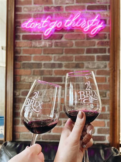 Two People Toasting Wine Glasses In Front Of A Brick Wall With Neon