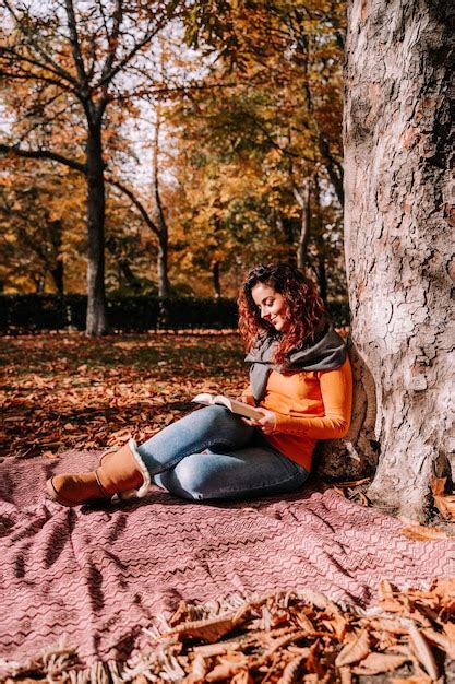 Premium Photo Smiling Woman Reading Book While Sitting By Tree Trunk