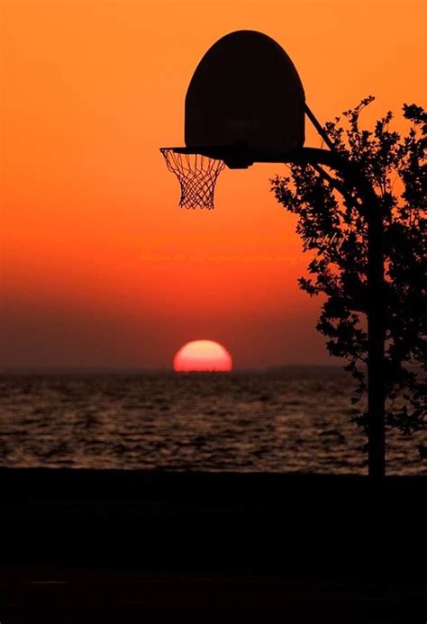 The Sun Is Setting Behind A Basketball Hoop In Front Of An Orange Sky