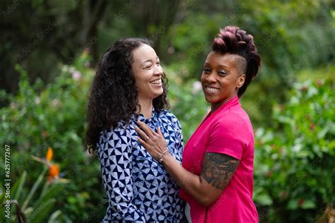 Two Women Stand Together Holding Each Other Close With Happy Smiles On Their Faces Adding