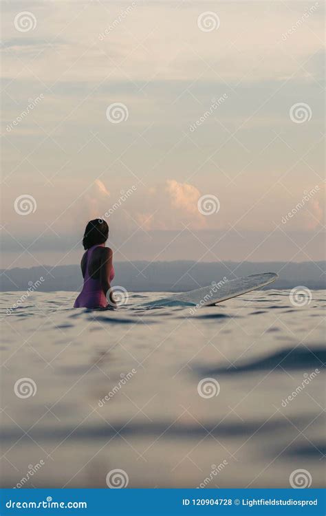 Back View Of Female Surfer Sitting On Surfboard In Water Stock Photo