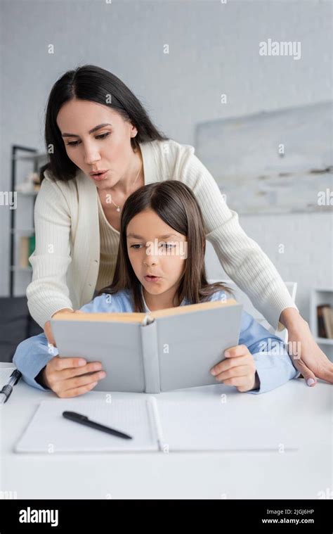 Brunette Nanny Helping Girl Reading Book While Doing Homework Stock