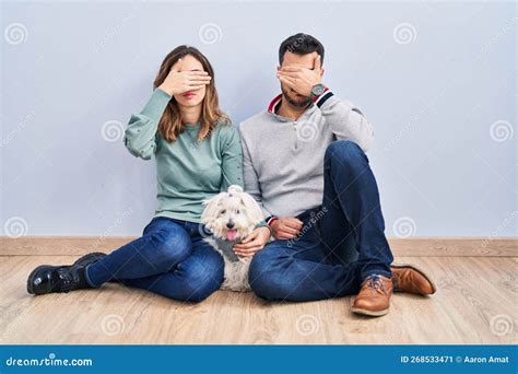 Young Hispanic Couple Sitting On The Floor With Dog Covering Eyes With