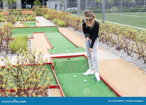 Woman Playing Mini Golf And Trying Putting Ball Into Hole Summer