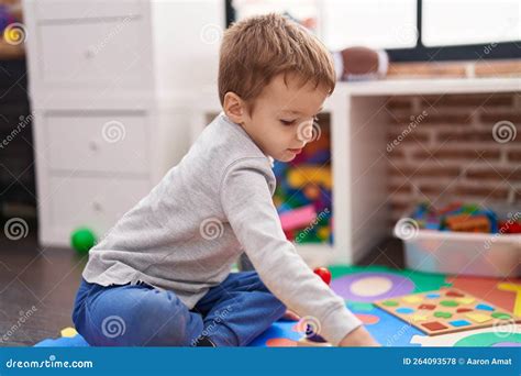 Adorable Toddler Sitting On Floor Playing At Kindergarten Stock Photo