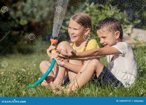 Enfants Heureux S Asseyant Sur L Herbe Et L Eau De Versement D Un Tuyau