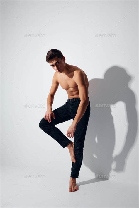 A Man With A Naked Torso Stands On His Leg Against A Light Background