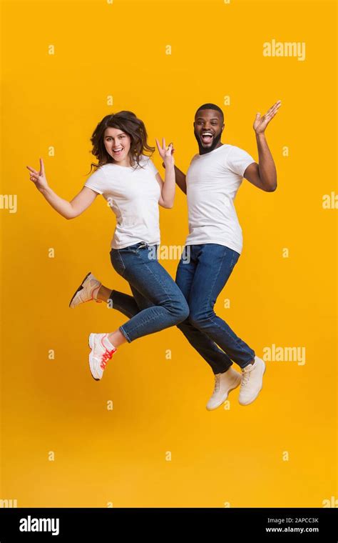 Playful Couple Having Fun Jumping In The Air Over Yellow Background