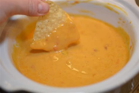 A Person Dipping Some Tortilla Chips Into A Bowl Of Orange Soup With Cheese