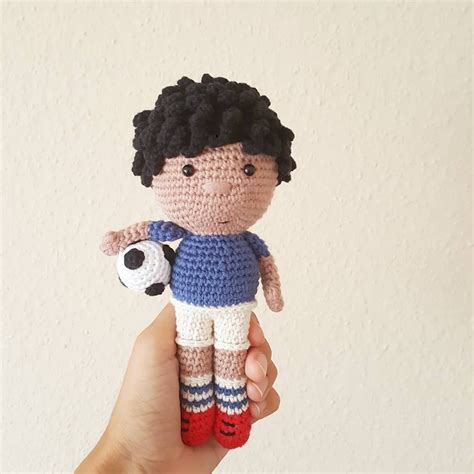 A Hand Holding A Small Crocheted Doll With A Soccer Ball In It S Left Hand