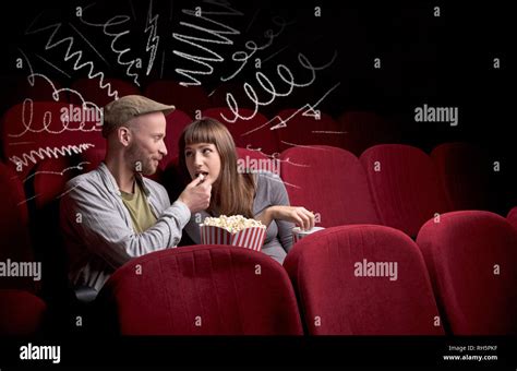 Young Cute Couple Sitting In Cinema And Eating Popcorn While Watching