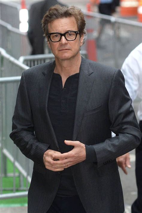 A Man Wearing Glasses And A Suit Walking Down The Street With His Hands