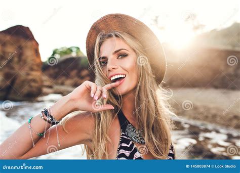 Portrait Of Attractive Blonde Girl With Long Hair Posing On Rocky Beach On Sunset Background