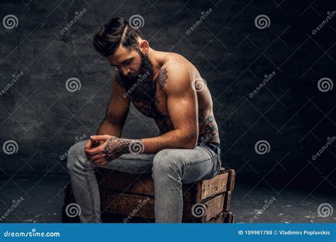 Bearded Male With Tattooed Torso Sits On A Wooden Box Stock Photo