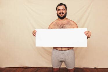 Portrait Of Naked Man Holding Blank Placard Against White Background