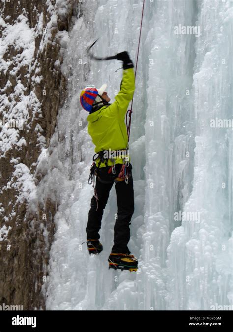 Male Ice Climber In A Yellow Jacket On A Steep Frozen Waterfall Ice