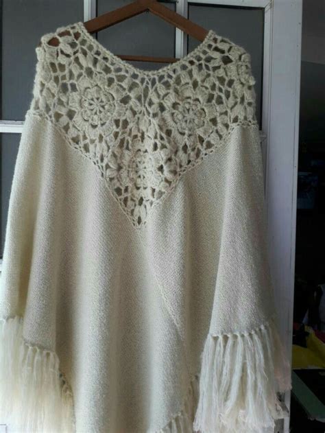 A White Sweater With Crochet And Tassels Hanging On A Hanger