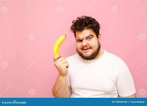 Funny Young Overweight Man Standing With A Banana In His Hand On A Pink