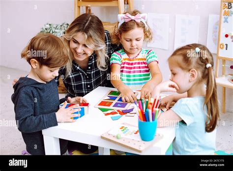 Niños pequeños y educador estudiando, doblando cubos y figuras geométricas de papel en el ...