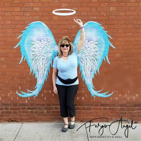 A Woman Standing In Front Of A Brick Wall With An Angel Painted On It