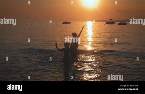 Silhouettes Mother And Daughter Sit On The Beach At Sunset Concept Of