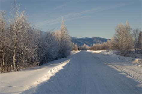 Estrada de terra coberta de neve para as montanhas muita neve e árvores