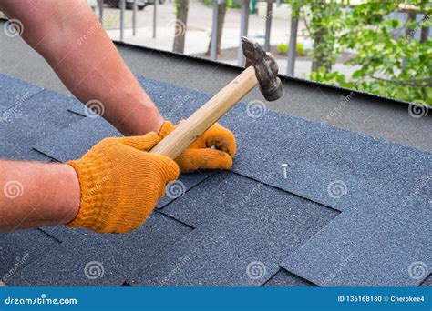 Workers Hands Installing Bitumen Roof Shingles Using Hammer In Nails