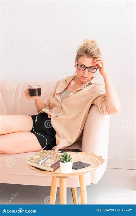 A Beautiful Woman In A Beige Shirt Sits Comfortably On The Sofa With