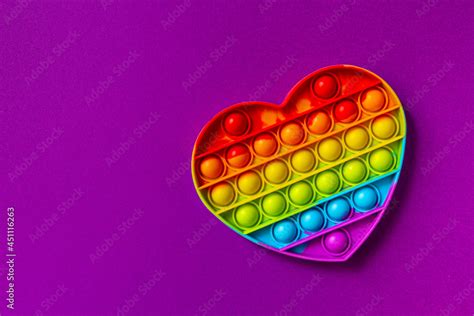 Pop it fidget toy on purple background with copy space. Rainbow heart anti stress fidget ...