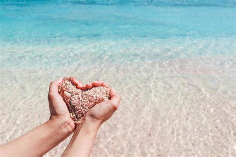 mano haciendo forma de corazón de arena rosa con agua transparente en