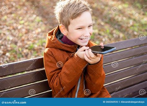 A Boy Records A Voice Message And Laughs While Sitting On A Park Bench