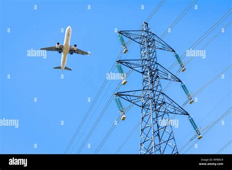 View from below of an airliner in landing approach flying over a high-voltage power line against ...