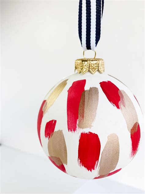 A White Ornament With Red And Gold Designs Hanging From A Blue Ribbon