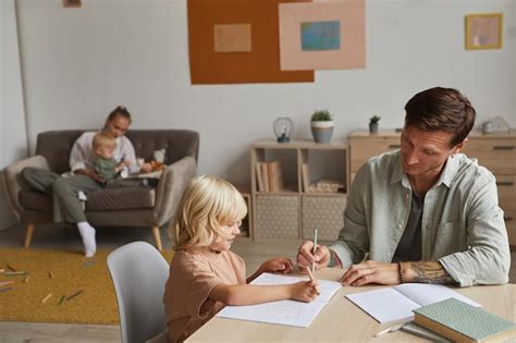 Premium Photo Father Helping His Son To Do His Homework At The Table With Mother Playing With