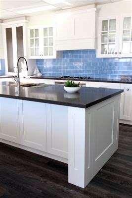 A White Kitchen With Blue Tile Backsplash And Black Counter Tops On