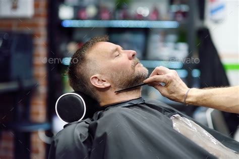 Barber Master Is Shaving Of Handsome Mature Bearded Man In Salon Hair Artist Making Hairstyle